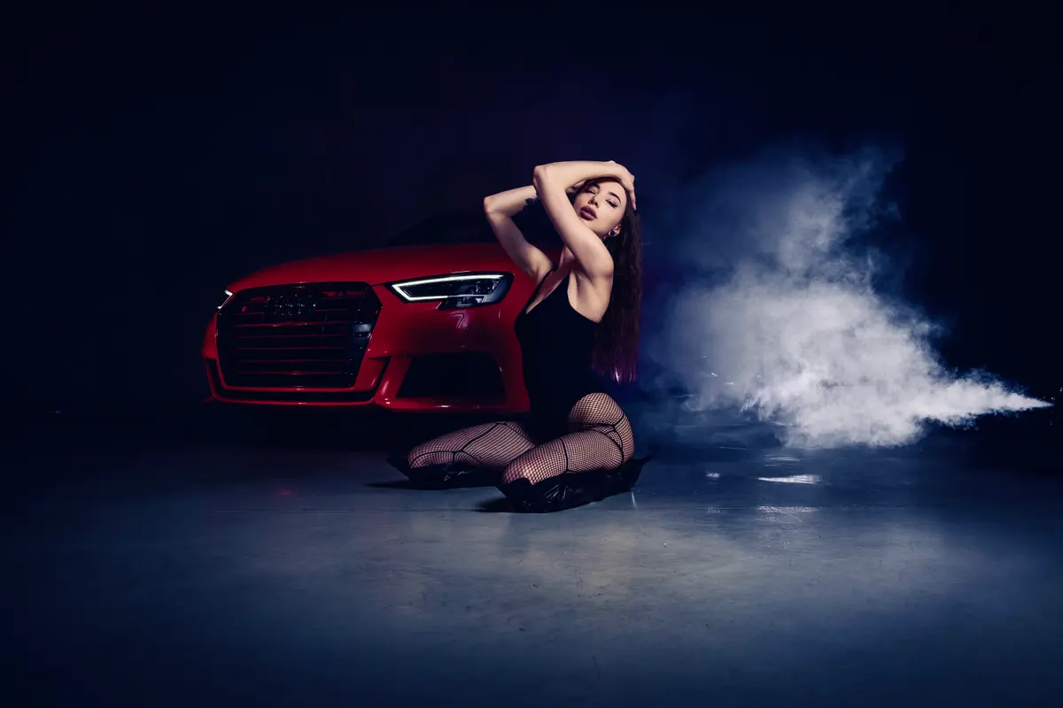 Woman kneeling in smoke beside red Audi S3 in studio