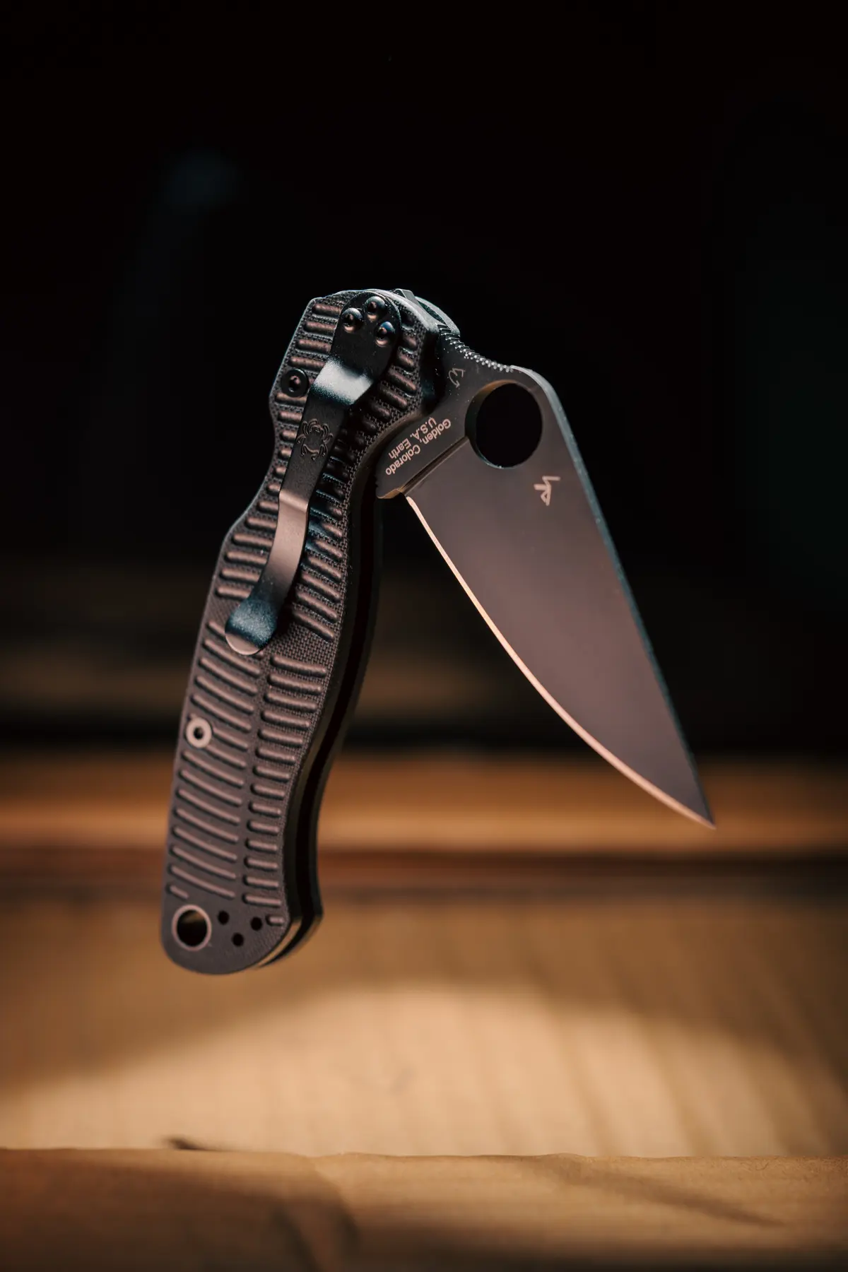 Black folding knife, blade open against dark wood background